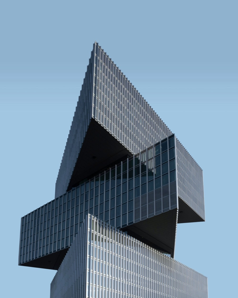 Modern tower made of stacked, offset glass sections against a pale blue sky